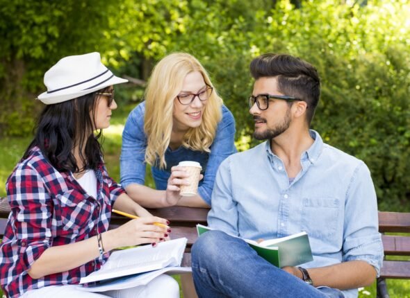 Group of young college students having fun while discussing homework on a park bench